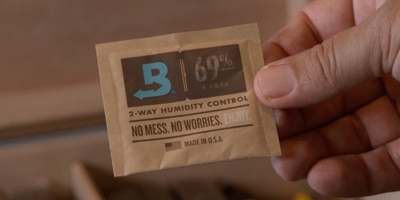 Hand holding a Boveda pack above box of cigars